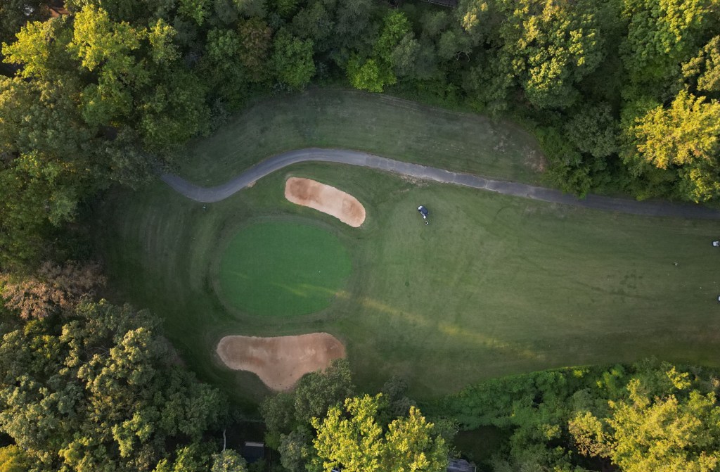 An aerial view of the golf course. Trees surround the hole as a golfer readies his round.